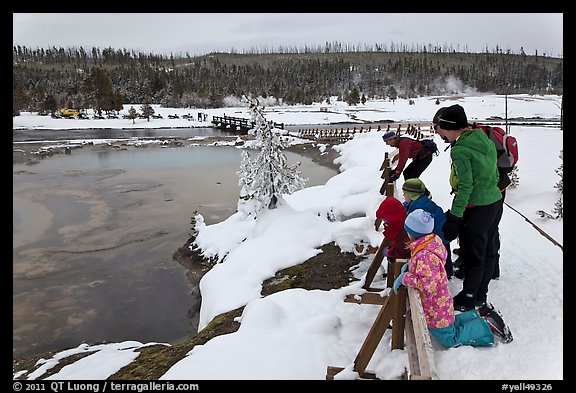 Family looks at thermal pool in winter. Yellowstone National Park, Wyoming, USA.