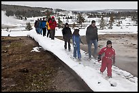 Tourists walk over snow-covered boardwalk. Yellowstone National Park, Wyoming, USA.