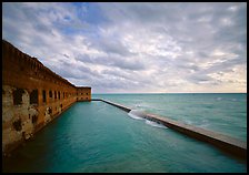 Fort Jefferson brick rampart and moat with wave over seawall, cloudy weather. Dry Tortugas National Park, Florida, USA.
