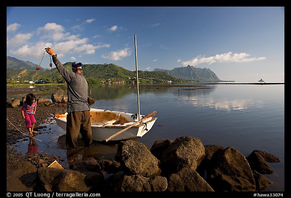 Fisherman pulling out fish out a net, with girl looking, Kaneohe Bay, morning. Oahu island, Hawaii, USA