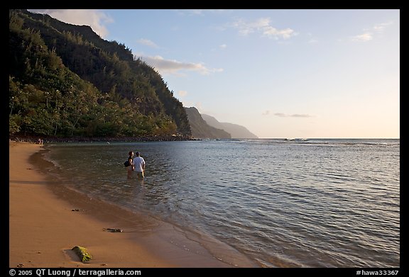 Couple standing in water looking at the Na Pali Coast, Kee Beach, late afternoon. Kauai island, Hawaii, USA