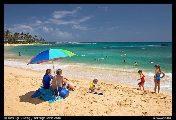 Couple sitting under sun unbrella with children playing around, Poipu Beach, mid-day. Kauai island, Hawaii, USA