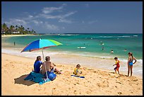 Couple sitting under sun unbrella with children playing around, Poipu Beach, mid-day. Kauai island, Hawaii, USA (color)
