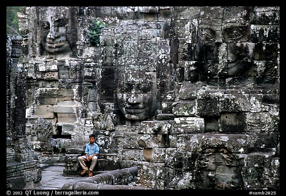 Boy sits next to large stone smiling faces, the Bayon. Angkor, Cambodia