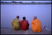 Buddhist monks sit on  banks of Tongle Sap river at dusk,  Phnom Phen. Cambodia