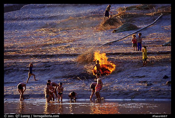 Children bathe in the river and dry out near a fire in a small hamlet. Mekong river, Laos (color)