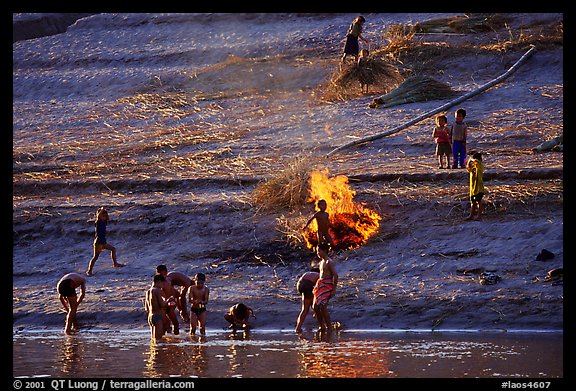 Children bathe in the river and dry out near a fire in a small hamlet. Mekong river, Laos