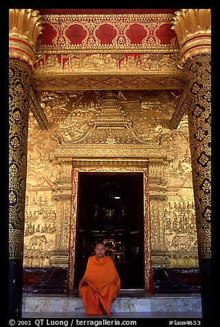 Buddhist novice monk sits at door of Wat Mai Suwannaphumaham. Luang Prabang, Laos