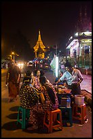 Women eating at street stall at night with Shwedagon Pagoda in background. Yangon, Myanmar
