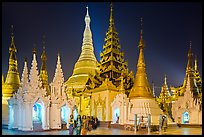 Women walking, stupas, shrines, and Main Stupa at night, Shwedagon Pagoda. Yangon, Myanmar ( color)