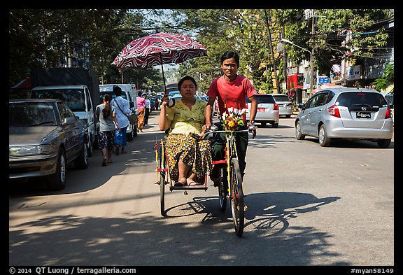 Woman holding unbrella against sun while riding Trishaw. Yangon, Myanmar