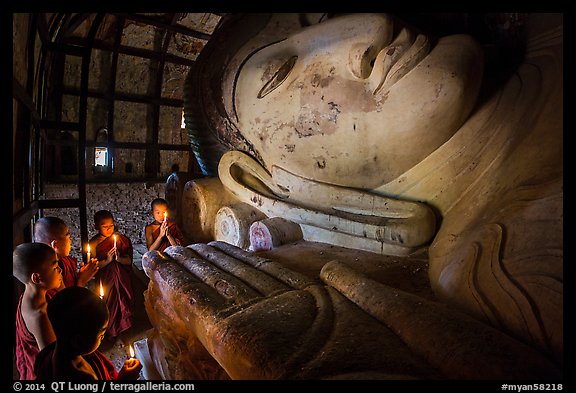 Young monks with candles worship Shin Bin Thal Yaung reclining Budddha. Bagan, Myanmar