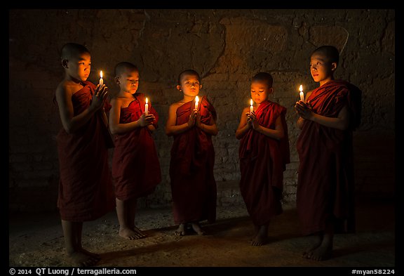 Five novices standing in circle inside temple with candles. Bagan, Myanmar (color)