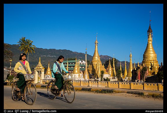 Schoolgirls riding bicycles past golden stupas. Pindaya, Myanmar (color)