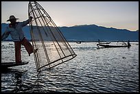 Intha fisherman standing on boat stern to lift net basket. Inle Lake, Myanmar ( color)
