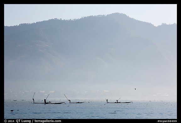 Intha fishermen in the distance using spears to stir fish, below tall hills. Inle Lake, Myanmar (color)