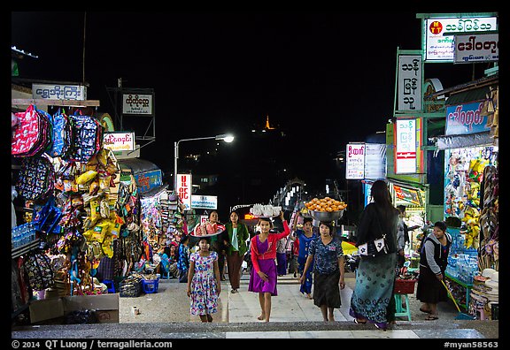 Girls carry offering material up the stairs of Potemkin village at night. Kyaiktiyo, Myanmar (color)