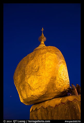 Pilgrims affix golden leaves to balancing boulder stupa at dawn. Kyaiktiyo, Myanmar (color)
