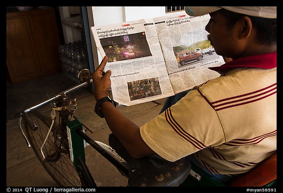 Cyclo driver looking at picture of QT Luong tour group in newspaper. Bago, Myanmar (color)
