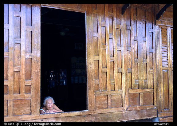 Woman looks out of teak house window. Damnoen Saduak, Thailand (color)