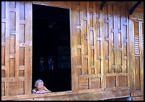 Woman looks out of teak house window. Damonoen Saduak, Thailand (color)
