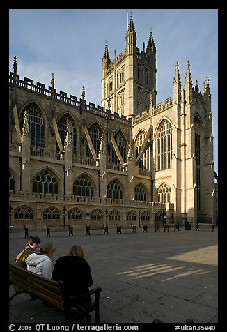Young people sitting on a bench in a square below Bath Abbey. Bath, Somerset, England, United Kingdom