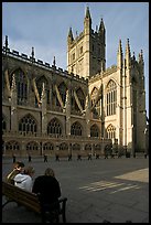 Young people sitting on a bench in a square below Bath Abbey. Bath, Somerset, England, United Kingdom