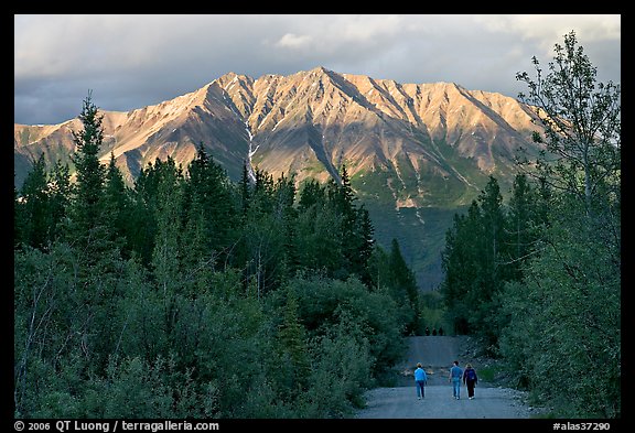 People walking on unpaved road, with last light on mountains. McCarthy, Alaska, USA (color)
