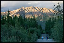 People walking on unpaved road, with last light on mountains. McCarthy, Alaska, USA