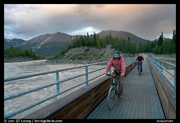 Mountain bikers crossing Kennicott River Footbridge at sunset. McCarthy, Alaska, USA (color)