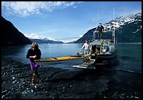 Man and woman carry kayak out of small boat at Black Sand Beach. Prince William Sound, Alaska, USA ( color)