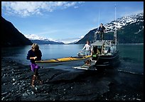 Man and woman carry kayak out of small boat at Black Sand Beach. Prince William Sound, Alaska, USA