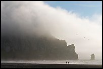 Two people strolling on the beach at the base of Morro Rock. Morro Bay, USA