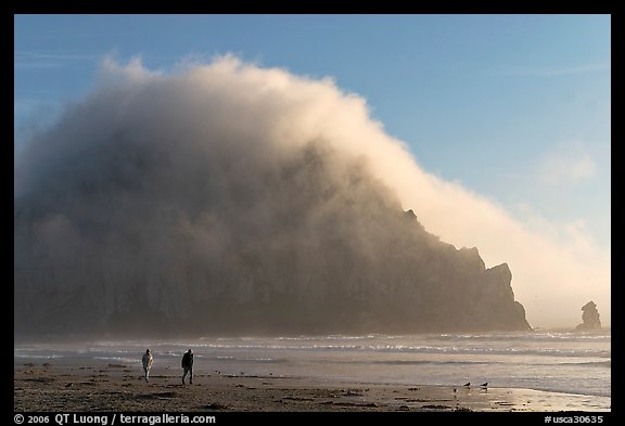 Couple walking on the beach, with Morro Rock and fog behind. Morro Bay, USA