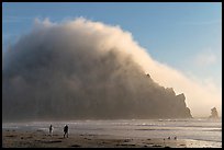 Couple walking on the beach, with Morro Rock and fog behind. Morro Bay, USA