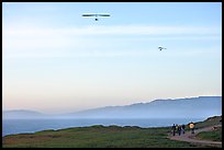 Hang gliders soaring above hikers, Fort Funston, late afternoon. San Francisco, California, USA