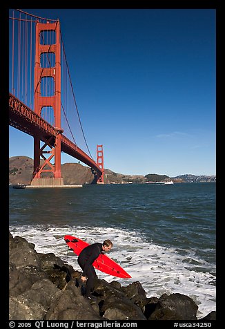 Surfer scrambling on rocks below the Golden Gate Bridge. San Francisco, California, USA (color)