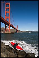 Surfer scrambling on rocks below the Golden Gate Bridge. San Francisco, California, USA