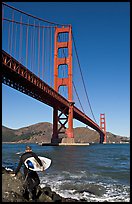 Surfer stepping on rocks and Golden Gate Bridge. San Francisco, California, USA