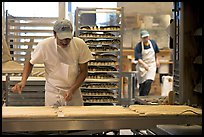 Baker hand-coating lofs of bread. San Francisco, California, USA (color)