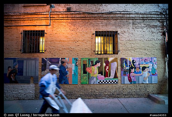 Man pushing a cart in front of mural paintings, Ross Alley, Chinatown. San Francisco, California, USA