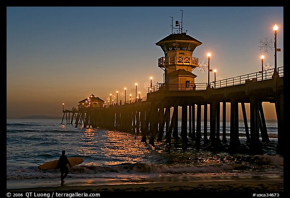 Surfer and Huntington Pier lights at twilight. Huntington Beach, Orange County, California, USA (color)