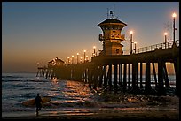Surfer and Huntington Pier lights at twilight. Huntington Beach, Orange County, California, USA