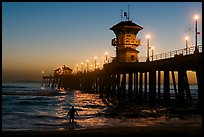 Surfer entering water next to the Huntington Pier, sunset. Huntington Beach, Orange County, California, USA (color)