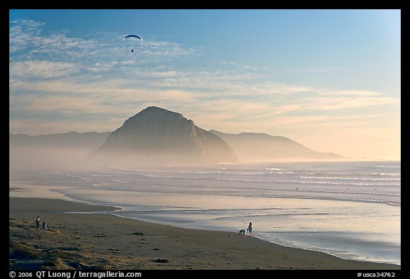 Motorized paraglider, women walking dog, with Morro Rock in the distance. Morro Bay, USA