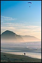 Motorized paraglider, women walking dog, and Morro Rock seen from Cayucos Beach. Morro Bay, USA