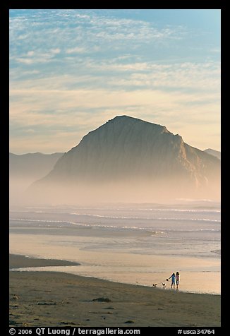 Women walking dog on the beach, with Morro Rock behind. Morro Bay, USA