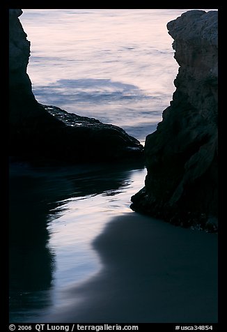 Reflection on wet sand through rock opening, Natural Bridges State Park, dusk. Santa Cruz, California, USA