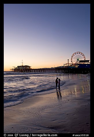 Couple standing on the beach at sunset, with pier and Ferris Wheel behind. Santa Monica, Los Angeles, California, USA