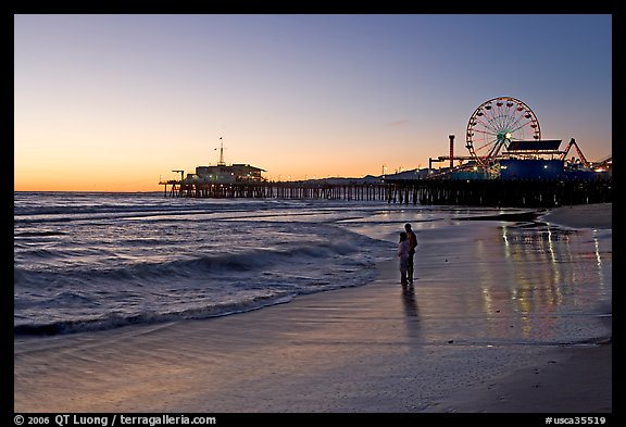 Couple reflected in wet sand at sunset, with pier and Ferris Wheel behind. Santa Monica, Los Angeles, California, USA (color)